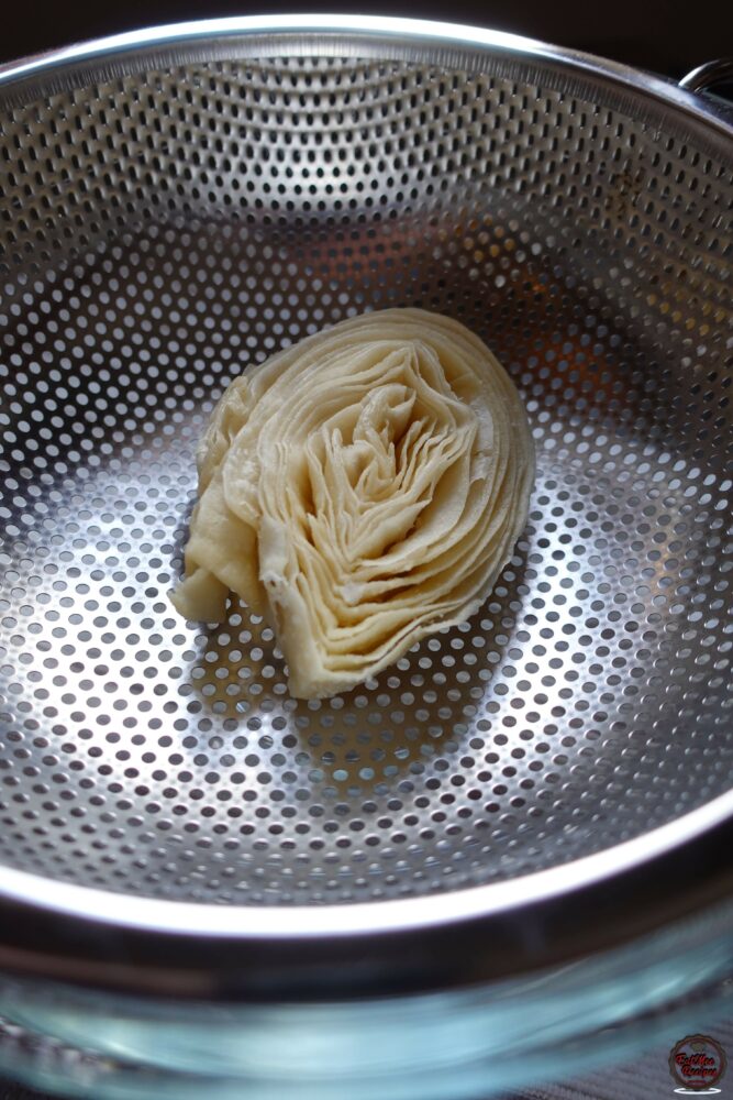 Once the syrup has cooled, place a strainer into a bowl & place one of the Banana Puri's onto the strainer.