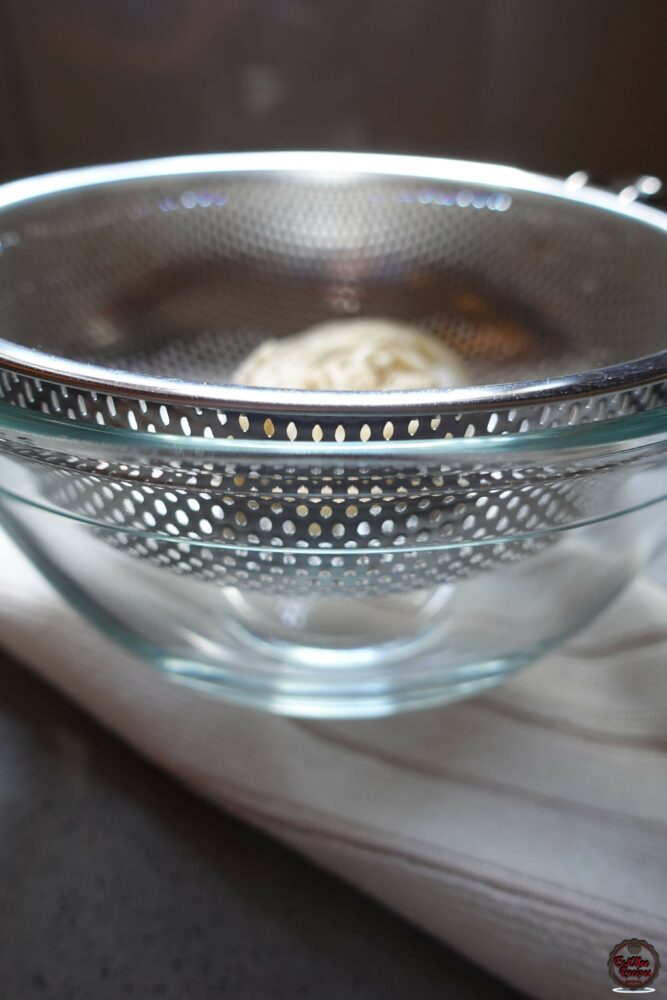 Once the syrup has cooled, place a strainer into a bowl & place one of the Banana Puri's onto the strainer.